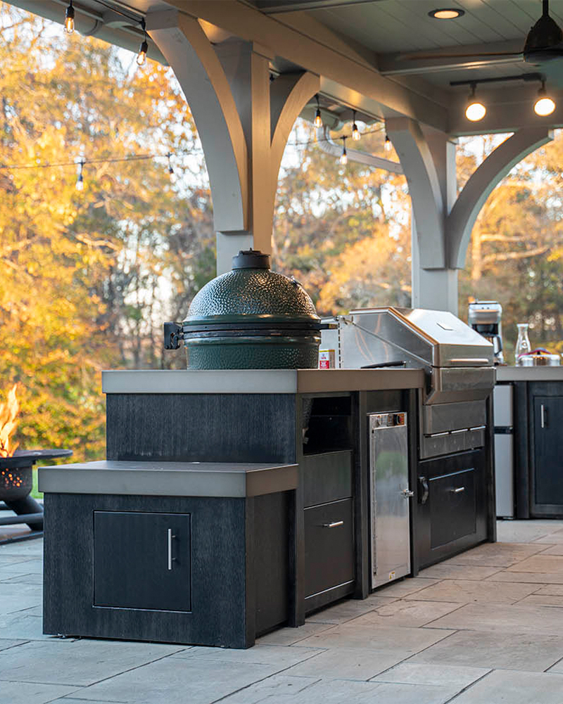 Covered outdoor kitchens island with kamado cooker, grill, and black cabinets.