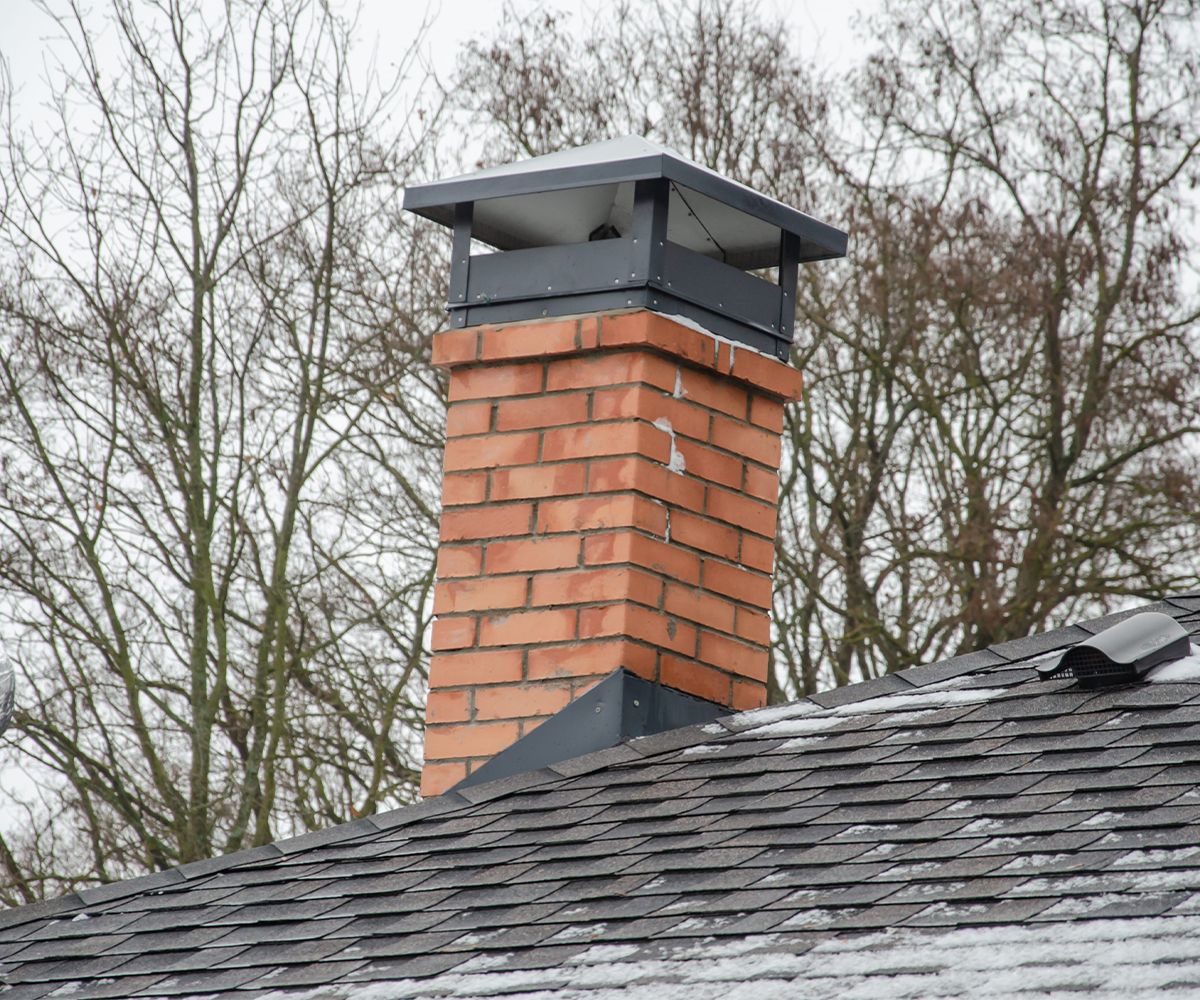 Brick chimney with metal cap protecting flue from rain, pests, and debris.