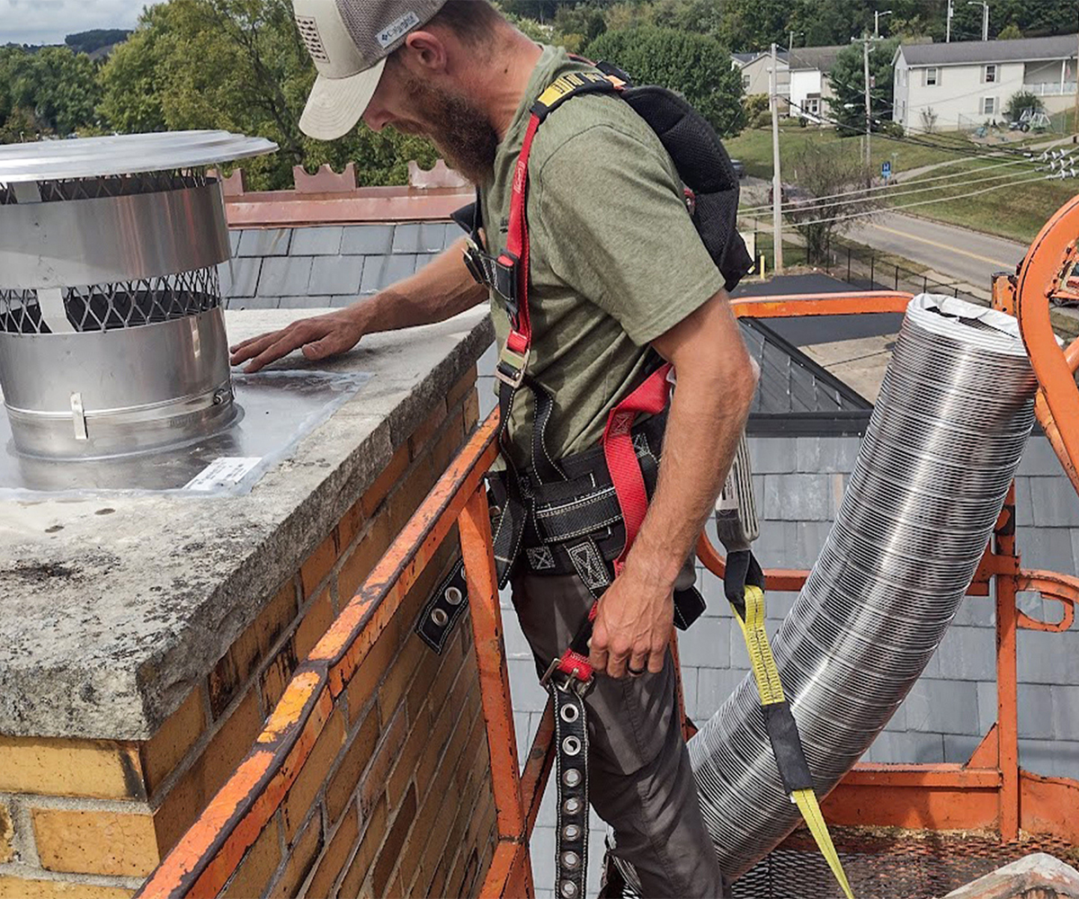 Technician inspects rooftop flue cap to maintain your chimney and prevent leaks.