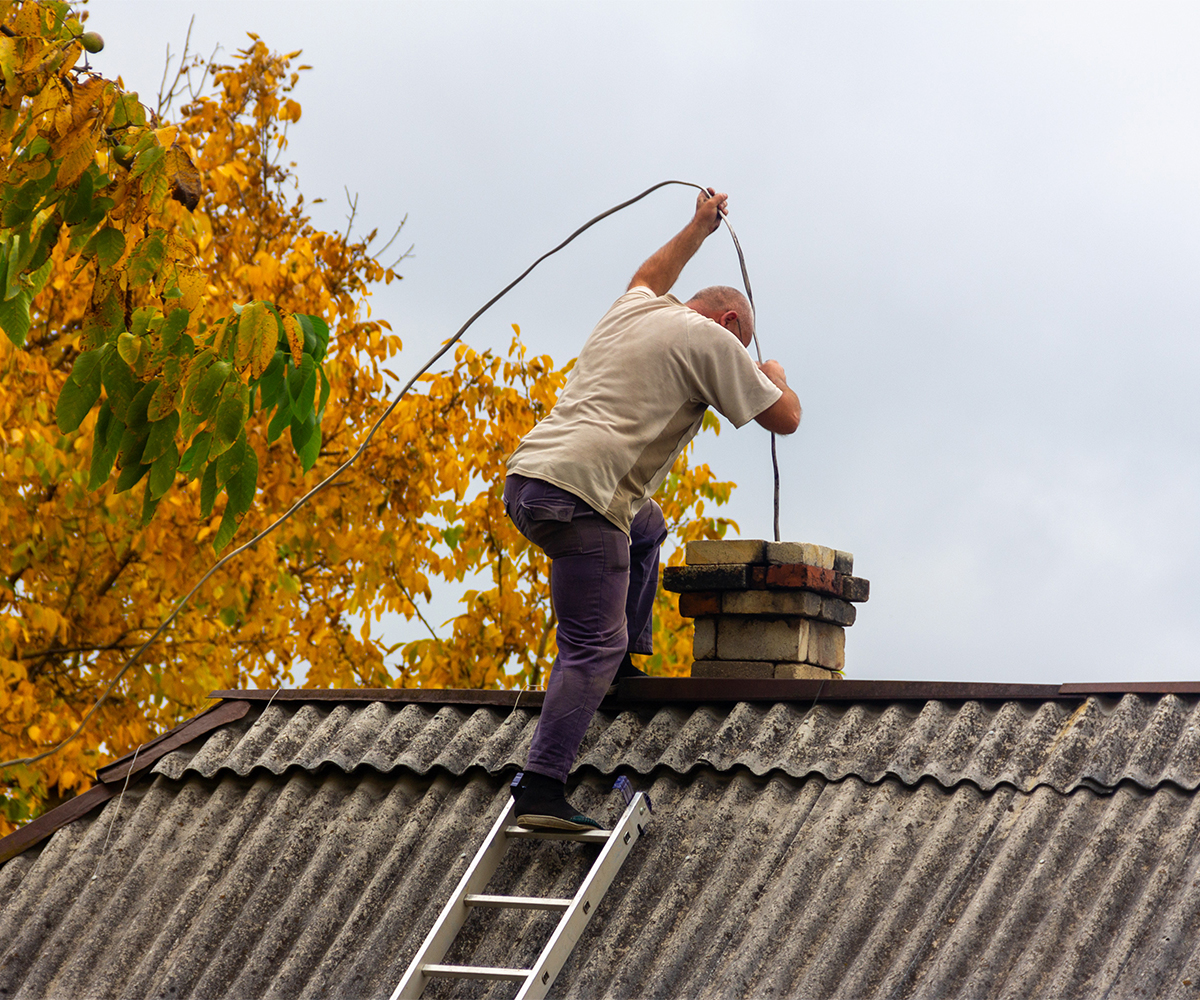 Chimney sweep clearing creosote from rooftop chimney with cleaning rods.