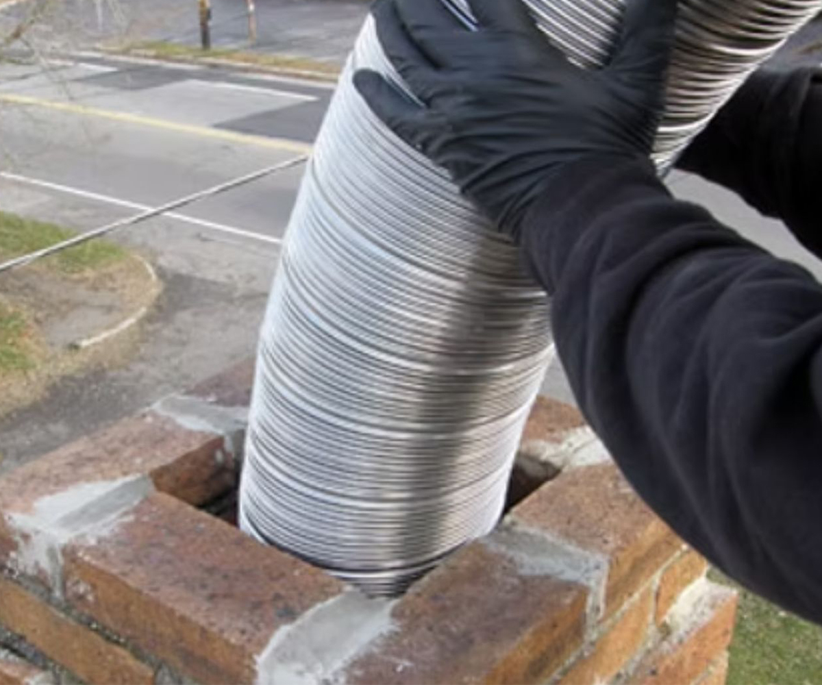 Technician feeds flexible stainless liner into brick chimney during relining.